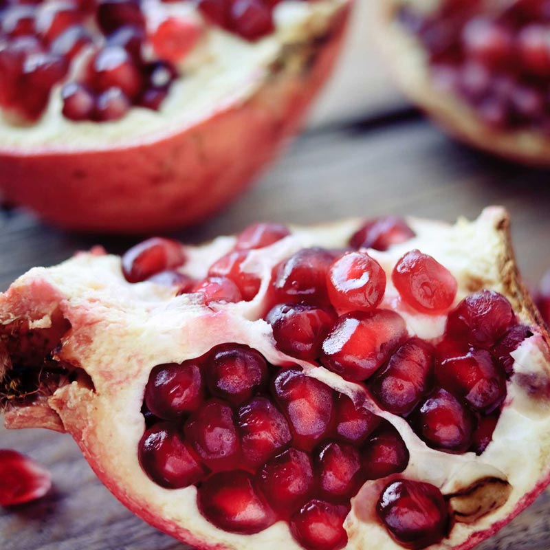 Pomegranate cut open to reveal juicy red seeds on a wooden surface.