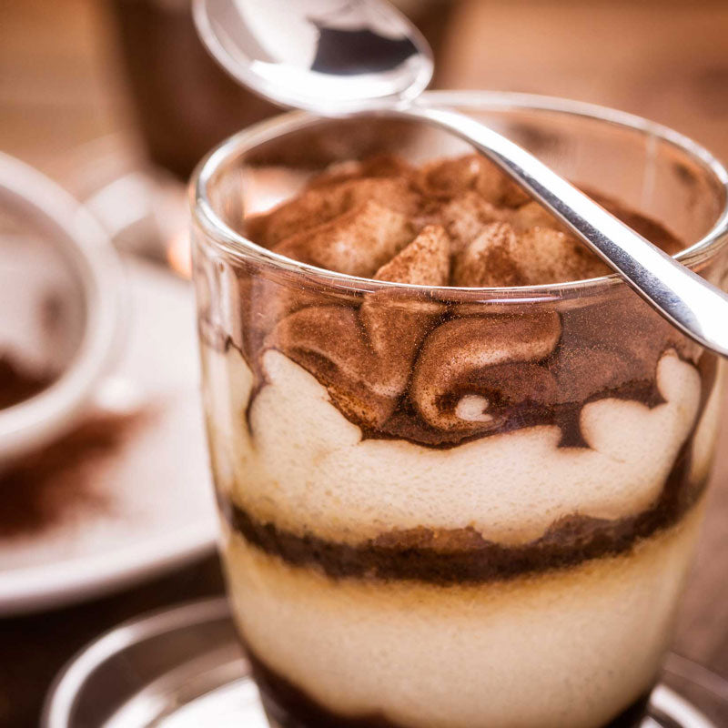 Close-up of a layered dessert in a glass with a spoon, blurred background