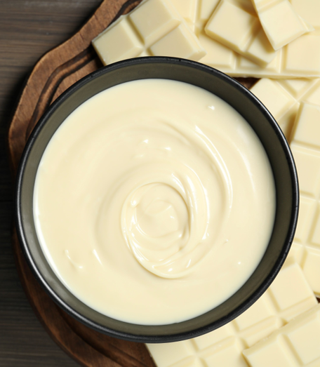 White chocolate ganache in a black bowl with white chocolate bars on a wooden surface