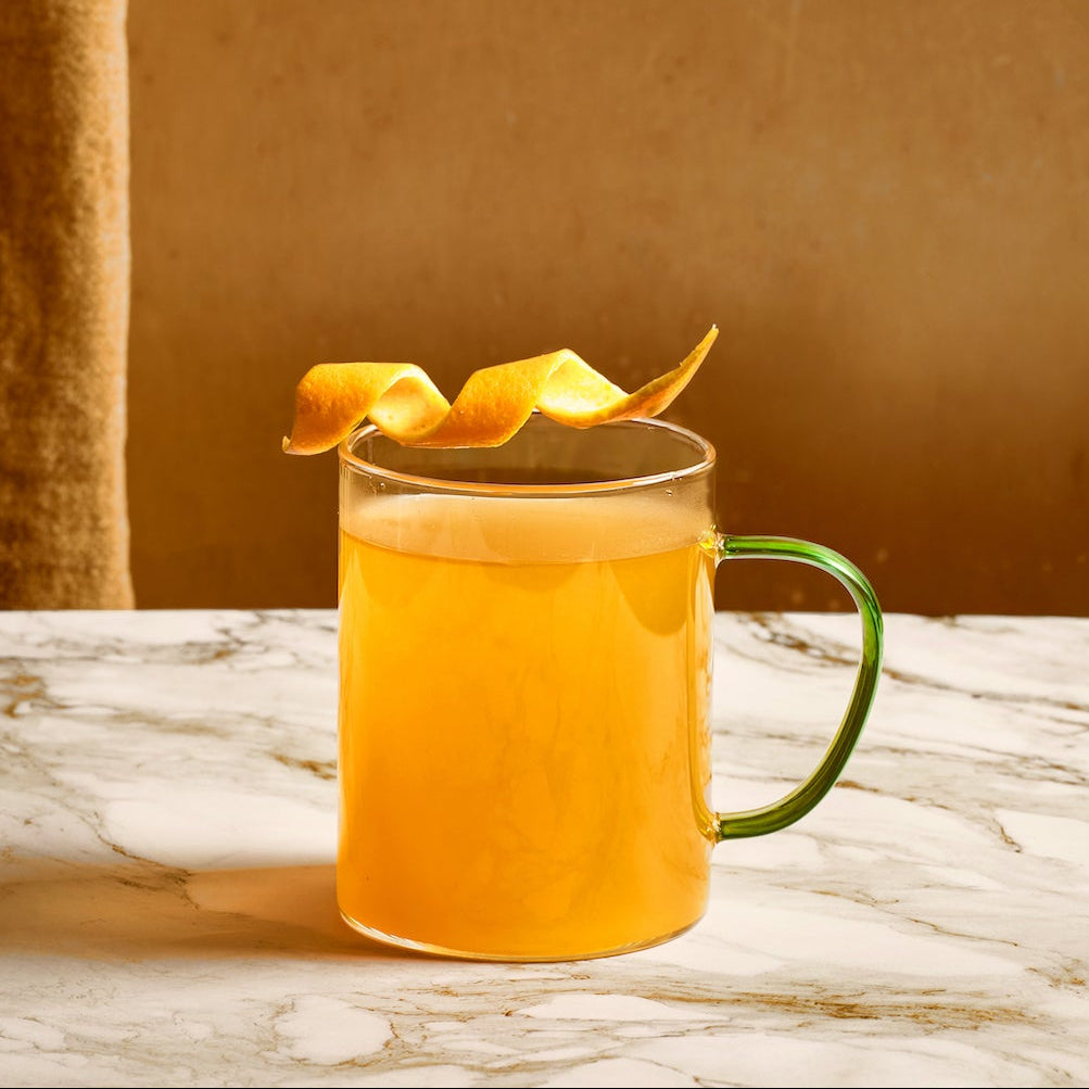 Glass of orange juice with a green handle on a marble surface against a brown curtain background