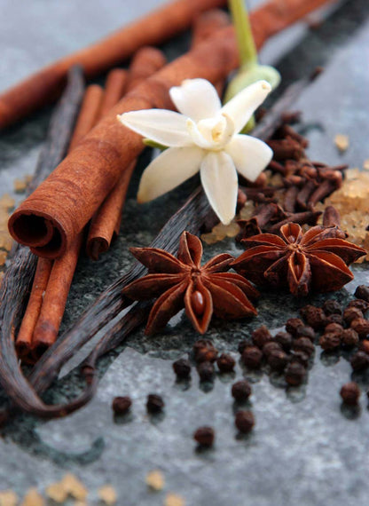 Spices including cinnamon sticks, star anise, and cloves on a dark surface with a white flower.
