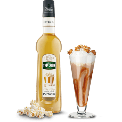 Bottle of Teisseire Pop Corn syrup with a glass of syrup and popcorn on a white background