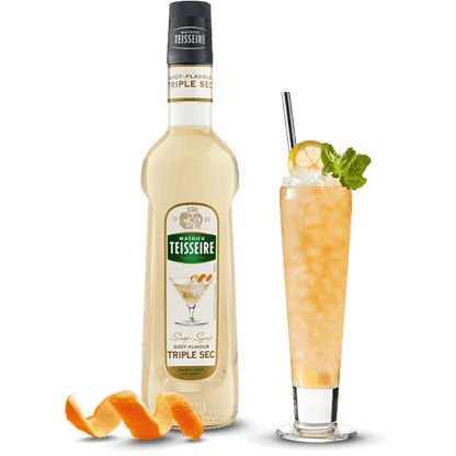 Bottle of Teisseire triple sec with a cocktail garnished with an orange peel and mint leaf on a white background