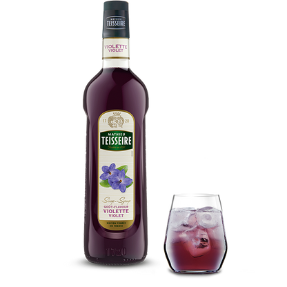 Bottle of Mathieu Teisseire Violette Violet syrup with a glass of the syrup on a white background