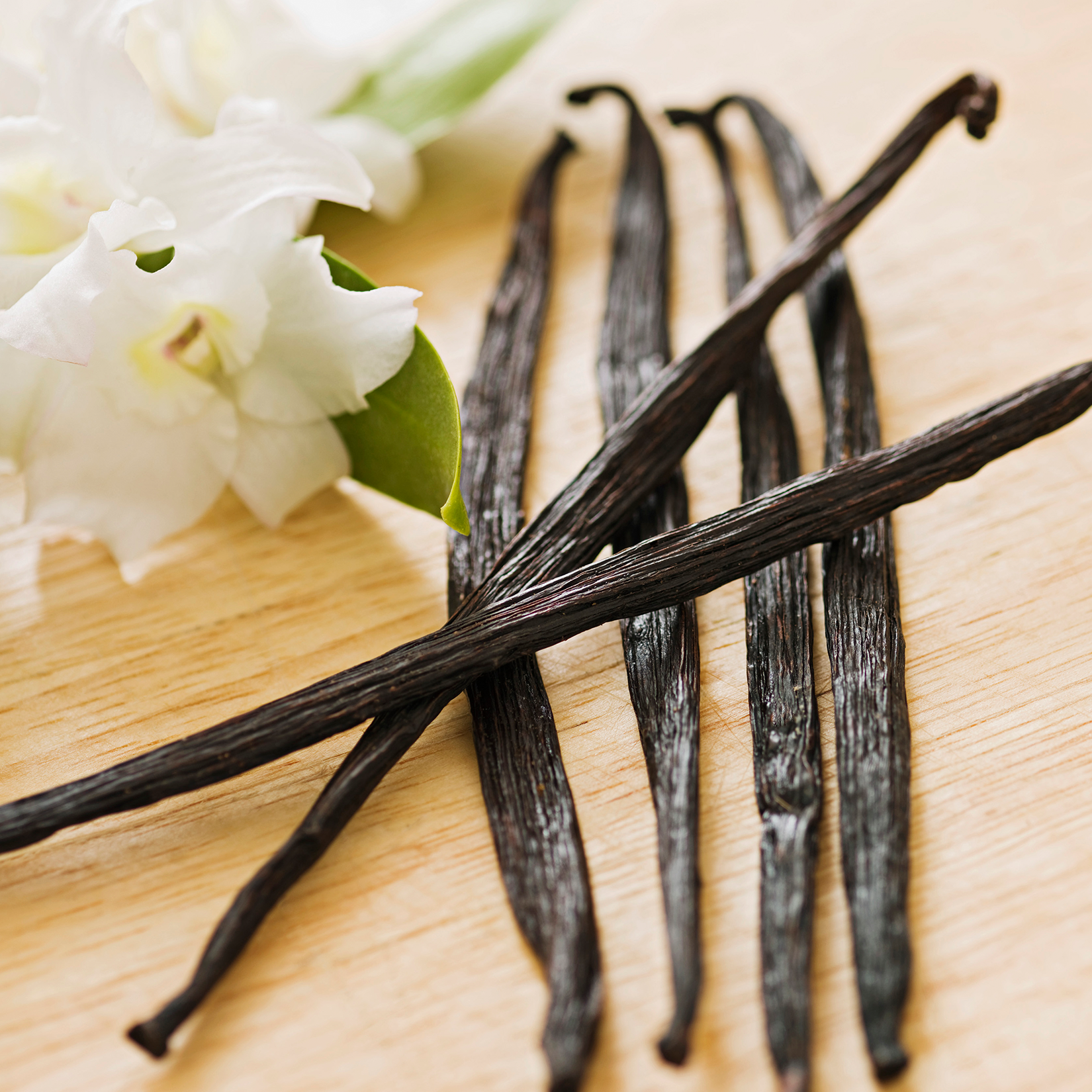 Vanilla beans on a wooden surface with white flowers in the background