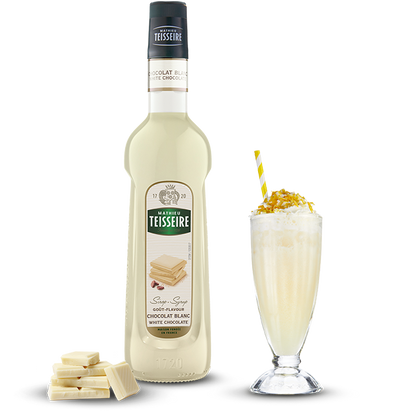Bottle of Teisseire white chocolate syrup with a glass of dessert and white chocolate pieces on a white background